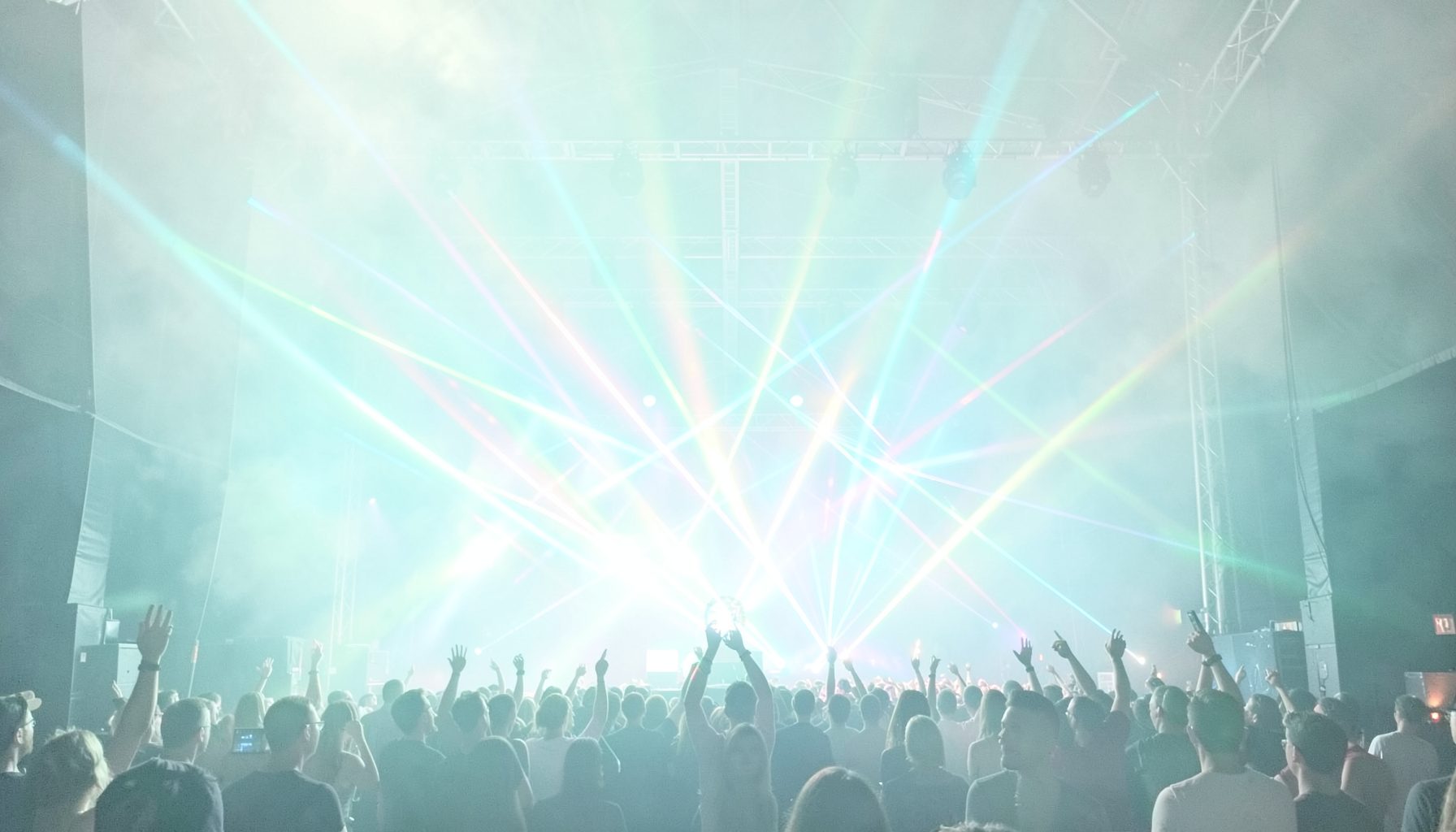 A bright concert stage with colorful laser lights cutting through haze, energetic and vibrant
