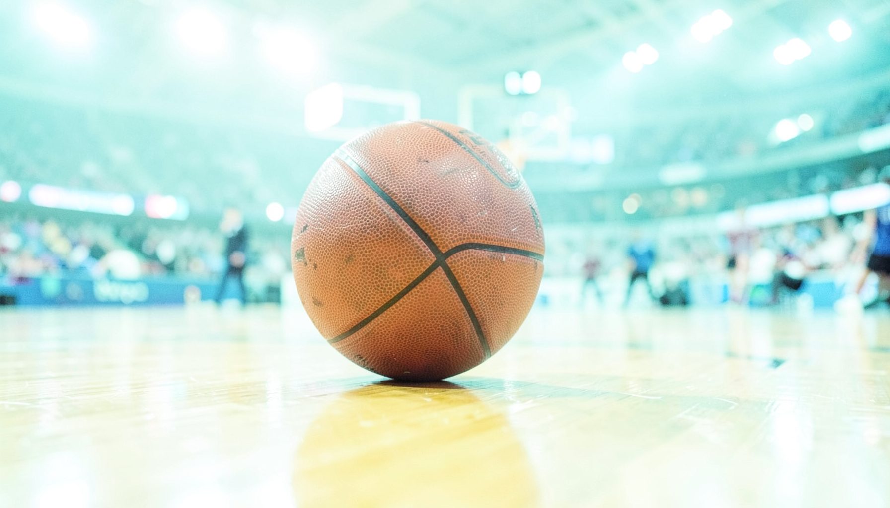 Close-up of a basketball resting on a polished wooden court, arena lights reflecting off the surface, intense game-day atmosphere