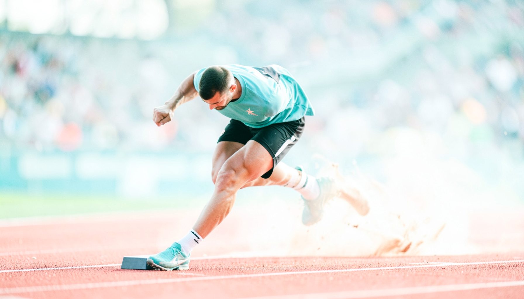 Sprinter exploding from the starting blocks on a red track, muscles tensed, stadium blurred in the background, peak athletic moment