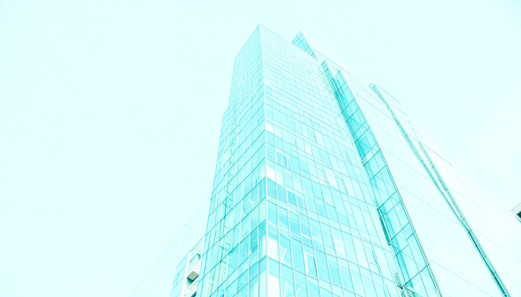 A bright high-key photograph of a modern glass office tower against a clear blue sky, conveying corporate ambition and economic energy.