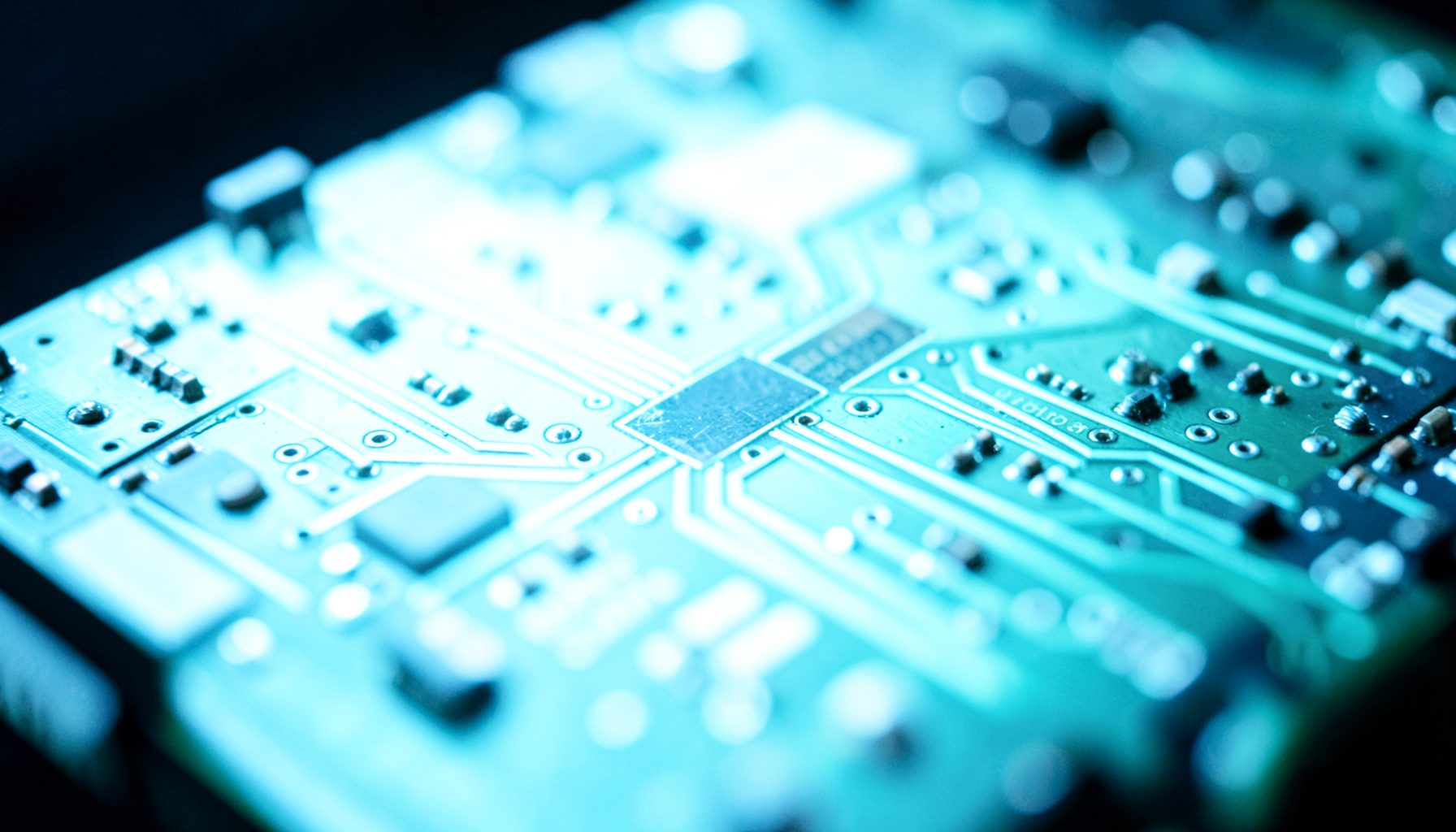 Close-up of a glowing circuit board with intricate copper traces and tiny components, bathed in cool blue and teal light against a dark background