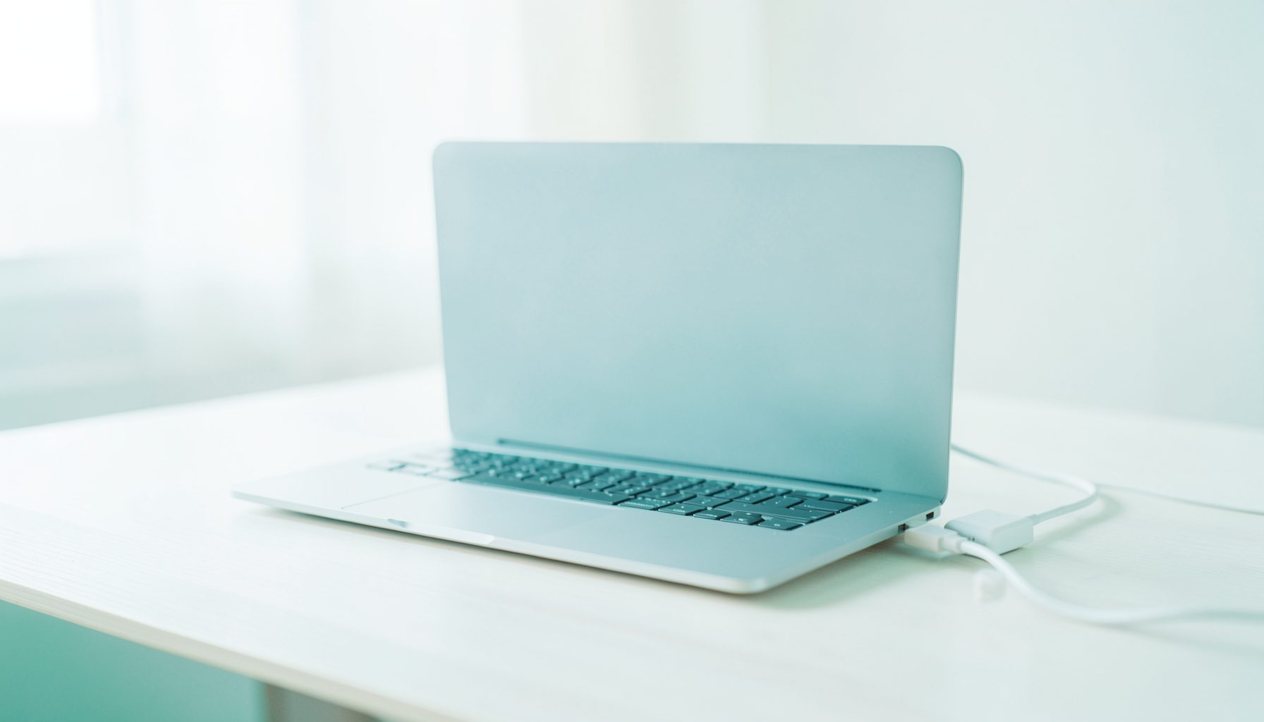 A MacBook Pro on a desk with its power adapter nearby, clean minimalist workspace in soft neutral tones